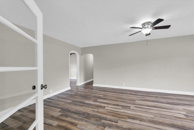 unfurnished room with dark wood-style flooring, a ceiling fan, baseboards, and arched walkways