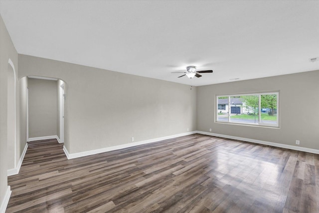 empty room with visible vents, baseboards, ceiling fan, dark wood-style floors, and arched walkways