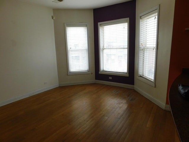 unfurnished room with hardwood / wood-style flooring, visible vents, and baseboards