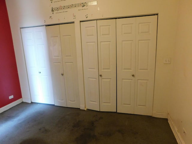 unfurnished bedroom with dark carpet, two closets, and baseboards