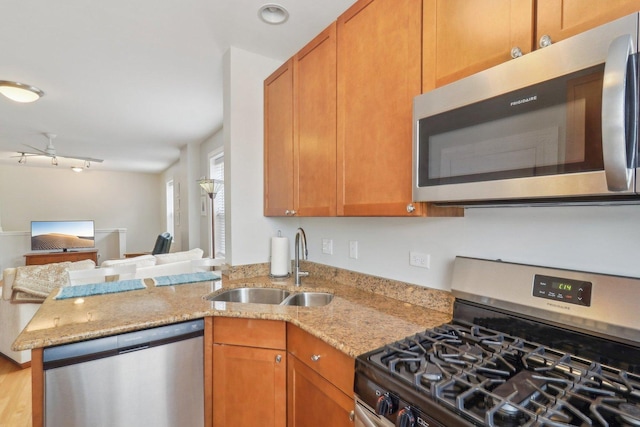 kitchen with light stone countertops, a peninsula, a sink, appliances with stainless steel finishes, and open floor plan