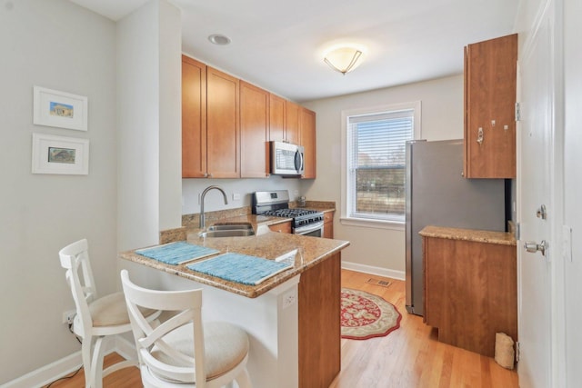 kitchen with light stone countertops, light wood-style flooring, a peninsula, stainless steel appliances, and a sink