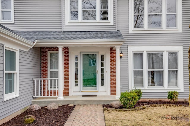 entrance to property featuring a shingled roof, a porch, and brick siding
