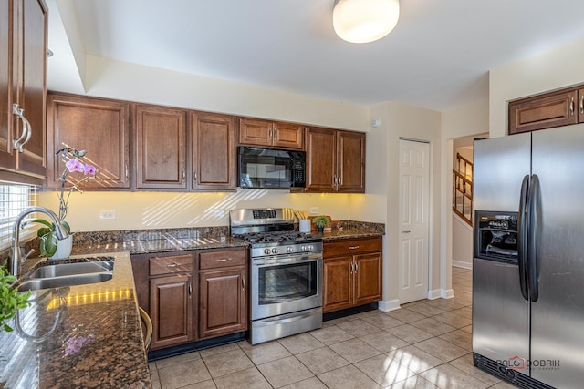 kitchen with a sink, dark stone countertops, appliances with stainless steel finishes, and light tile patterned floors
