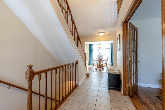 corridor with light tile patterned flooring, baseboards, a chandelier, and stairway
