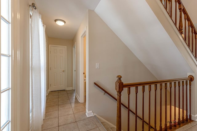 hall with light tile patterned flooring, an upstairs landing, baseboards, and a healthy amount of sunlight