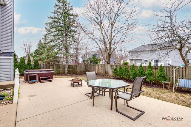 view of patio featuring a hot tub, an outdoor fire pit, a fenced backyard, and outdoor dining area