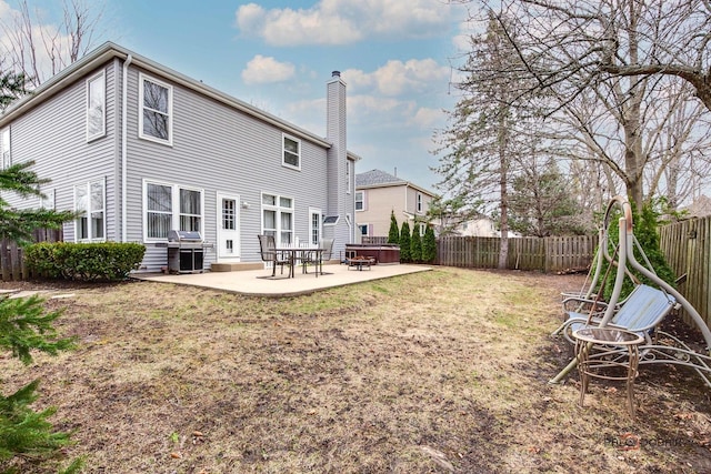 rear view of property featuring entry steps, a chimney, a fenced backyard, a lawn, and a patio area