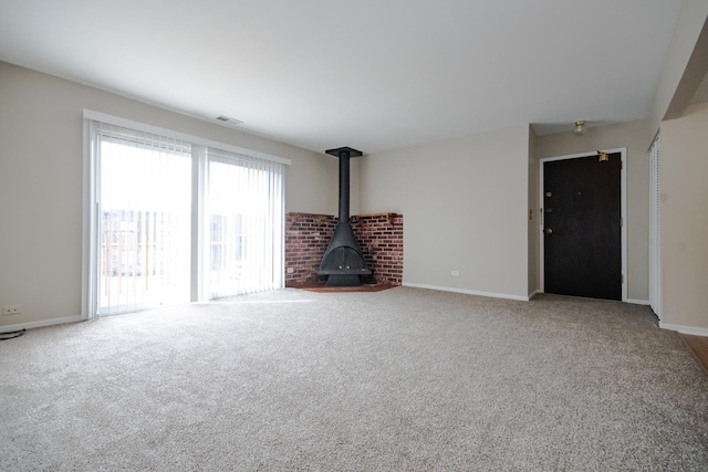 unfurnished living room featuring carpet floors, baseboards, a wood stove, and visible vents