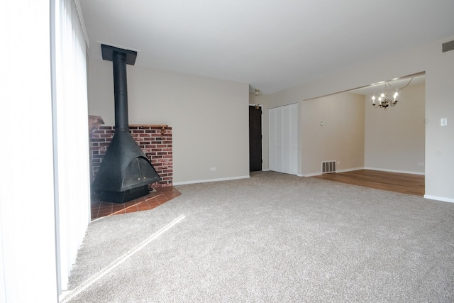 unfurnished living room featuring a chandelier, carpet floors, a wood stove, and visible vents