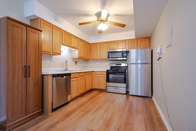 kitchen featuring light countertops, a sink, ceiling fan, light wood-style flooring, and appliances with stainless steel finishes