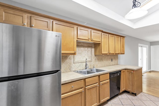 kitchen featuring freestanding refrigerator, black dishwasher, a sink, light countertops, and backsplash