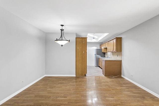 kitchen featuring freestanding refrigerator, light wood-style flooring, light countertops, backsplash, and baseboards