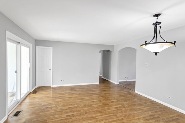 unfurnished room featuring arched walkways, light wood-type flooring, and baseboards