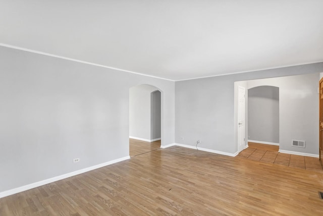 empty room featuring arched walkways, light wood-type flooring, baseboards, and crown molding