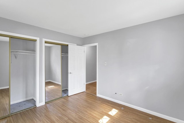 unfurnished bedroom featuring two closets, baseboards, and wood finished floors