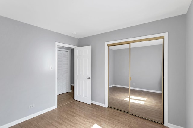 unfurnished bedroom featuring baseboards, light wood-type flooring, and a closet