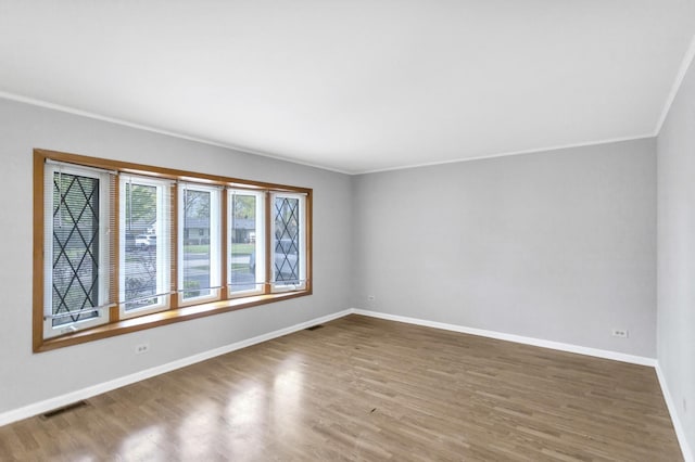 spare room with wood finished floors, crown molding, and baseboards