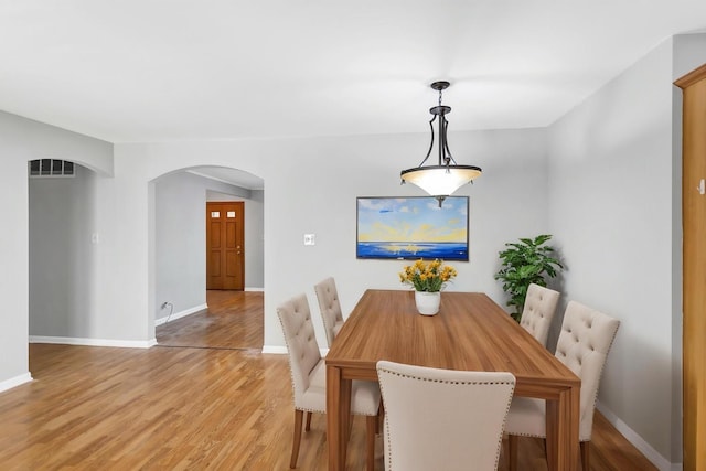 dining area with arched walkways, light wood-style flooring, and baseboards