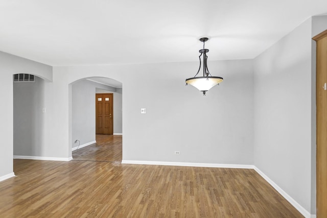 spare room featuring arched walkways, baseboards, and wood finished floors
