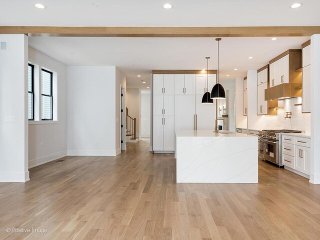 2141 W Grace St, Chicago, IL 60618 - kitchen featuring range with two ovens, a spacious island, light wood finished floors, white cabinetry, and hanging light fixtures