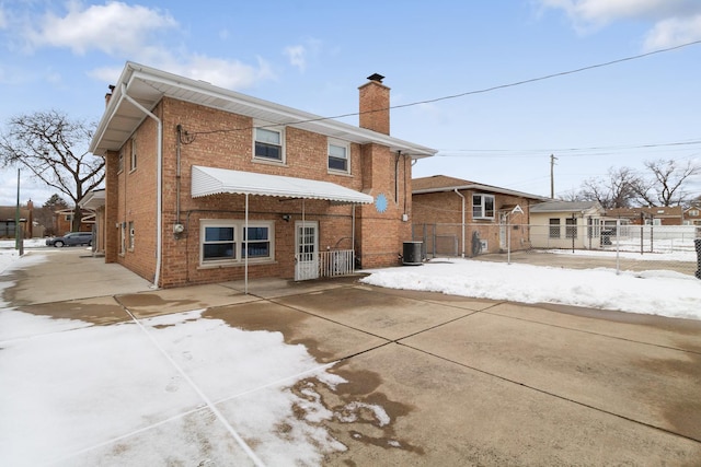 snow covered house featuring brick siding, fence, and cooling unit