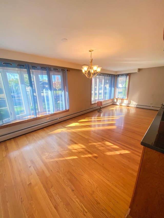 empty room featuring a chandelier, a baseboard radiator, and wood finished floors