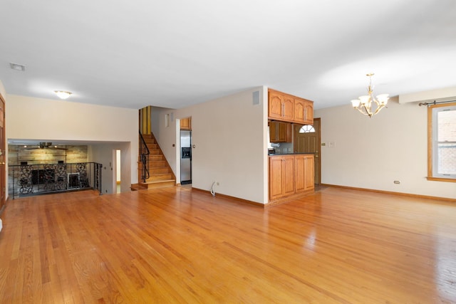 unfurnished living room with baseboards, a chandelier, a fireplace, stairway, and light wood-style flooring