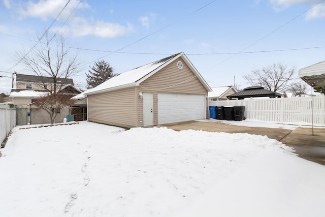 snow covered garage with a garage and fence