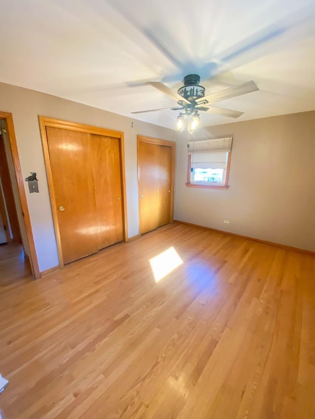 unfurnished bedroom with multiple closets, light wood-type flooring, ceiling fan, and baseboards