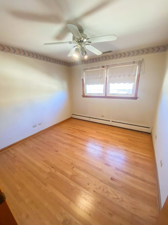 unfurnished room featuring baseboard heating, light wood-type flooring, and baseboards