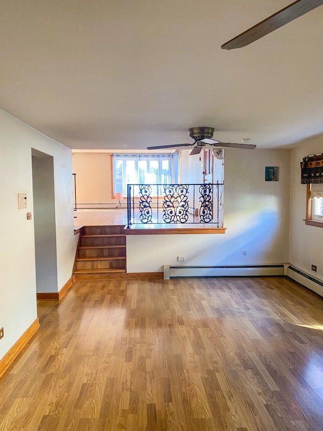 unfurnished room with wood finished floors, baseboards, a ceiling fan, and stairs