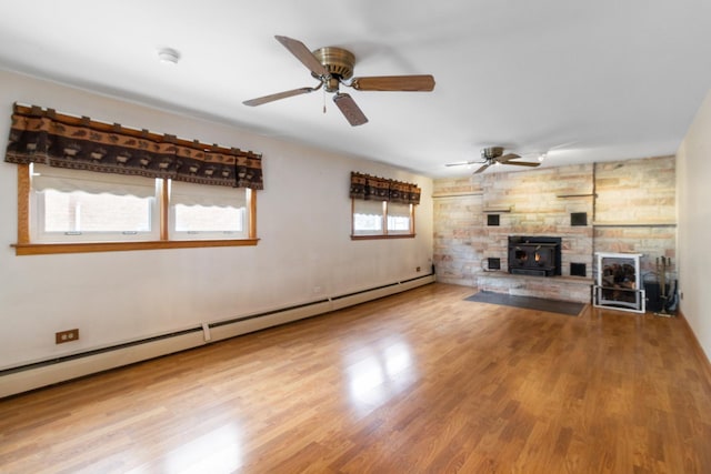 unfurnished living room featuring a wood stove, a baseboard heating unit, a ceiling fan, and wood finished floors