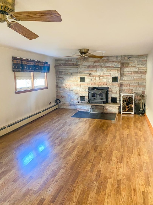 unfurnished living room with a wood stove, ceiling fan, a baseboard radiator, and wood finished floors