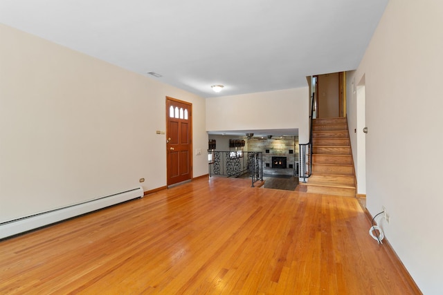 unfurnished living room with light wood-style floors, visible vents, a warm lit fireplace, stairs, and a baseboard radiator