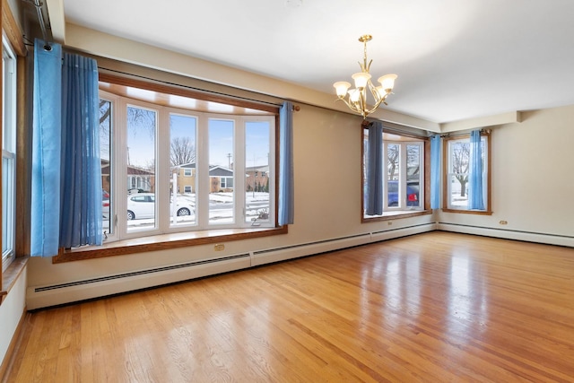 empty room featuring wood finished floors, a baseboard heating unit, and an inviting chandelier