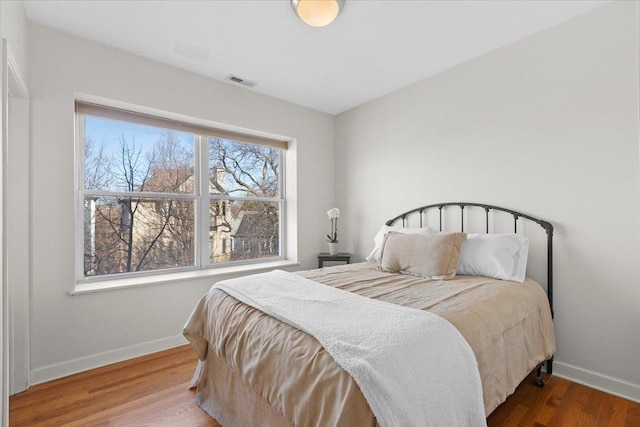 bedroom with wood finished floors, visible vents, and baseboards