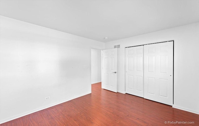 unfurnished bedroom featuring baseboards, dark wood-style flooring, visible vents, and a closet