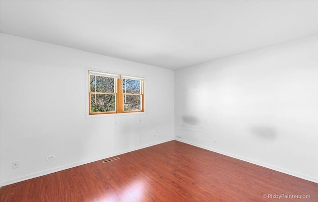 empty room featuring baseboards, visible vents, and wood finished floors