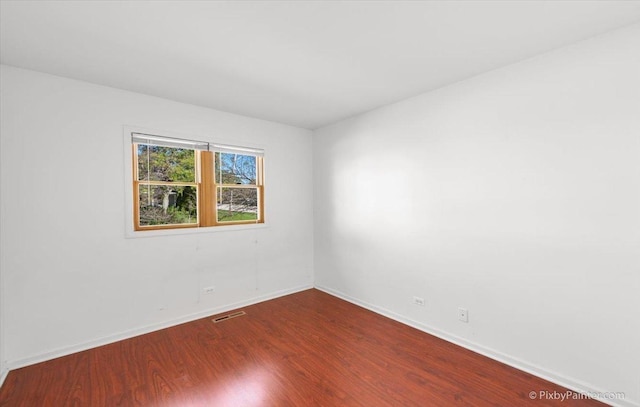 empty room featuring baseboards, visible vents, and wood finished floors