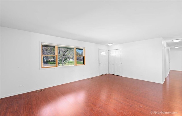 unfurnished living room with baseboards, visible vents, and wood finished floors