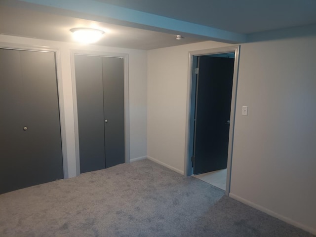unfurnished bedroom featuring baseboards, carpet flooring, and two closets