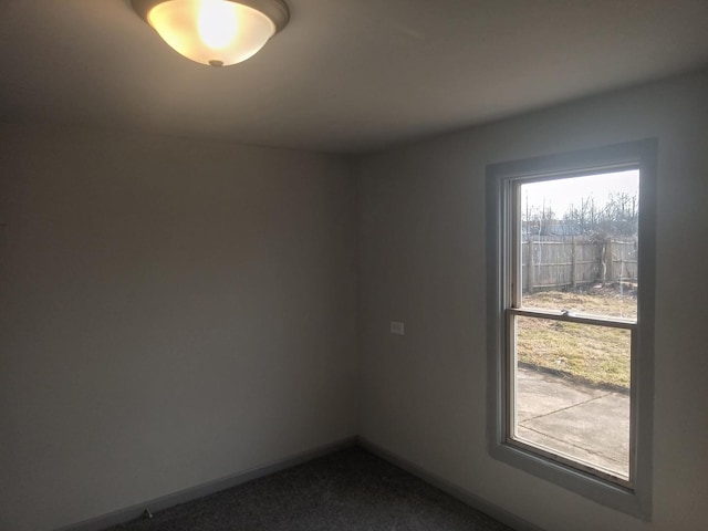 spare room featuring dark carpet and baseboards