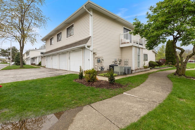 view of side of property featuring aphalt driveway, a lawn, a balcony, central AC, and an attached garage
