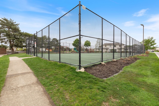 view of tennis court featuring a lawn and fence