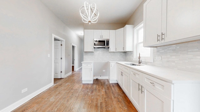 kitchen featuring light wood-type flooring, a sink, stainless steel microwave, decorative backsplash, and a chandelier