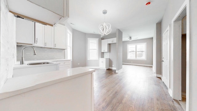kitchen featuring light wood-type flooring, a notable chandelier, a sink, white cabinets, and decorative backsplash