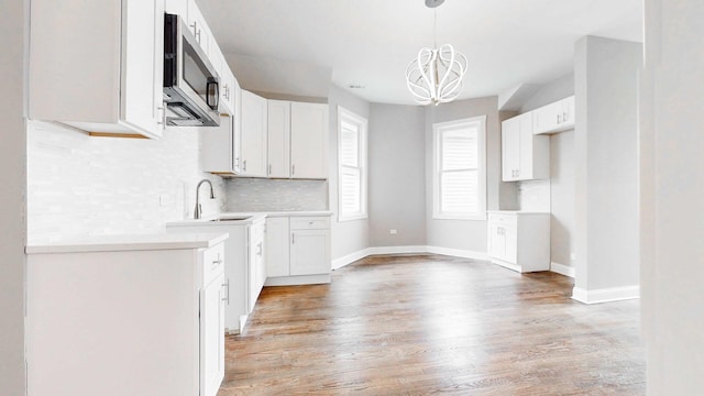 kitchen with stainless steel microwave, a chandelier, decorative backsplash, light wood-style floors, and a sink