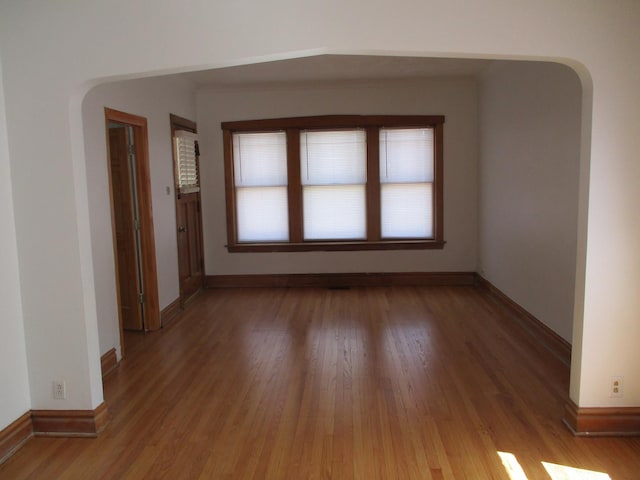 unfurnished room featuring light wood-style flooring, baseboards, and arched walkways