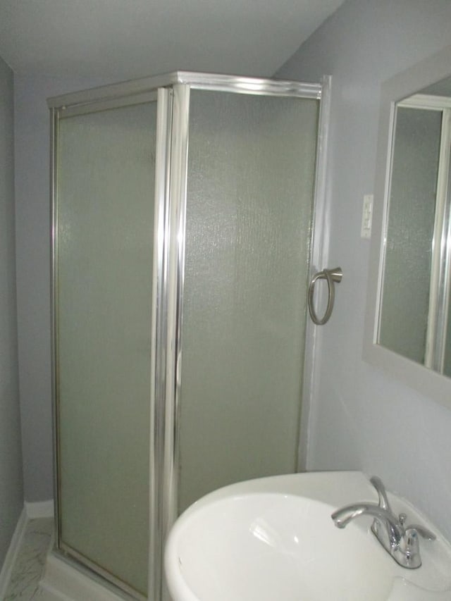 bathroom featuring marble finish floor, a stall shower, and a sink